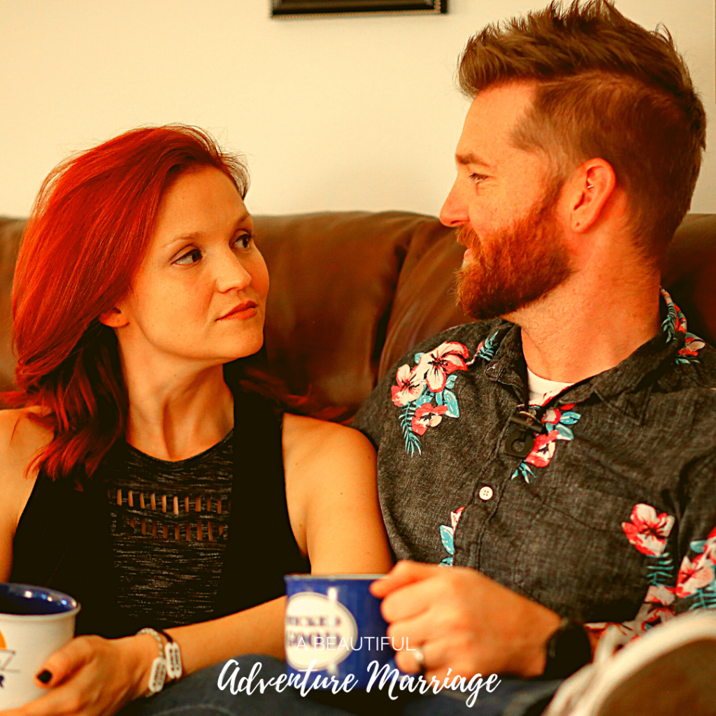 a couple sitting on the couch holding coffee cups talking
