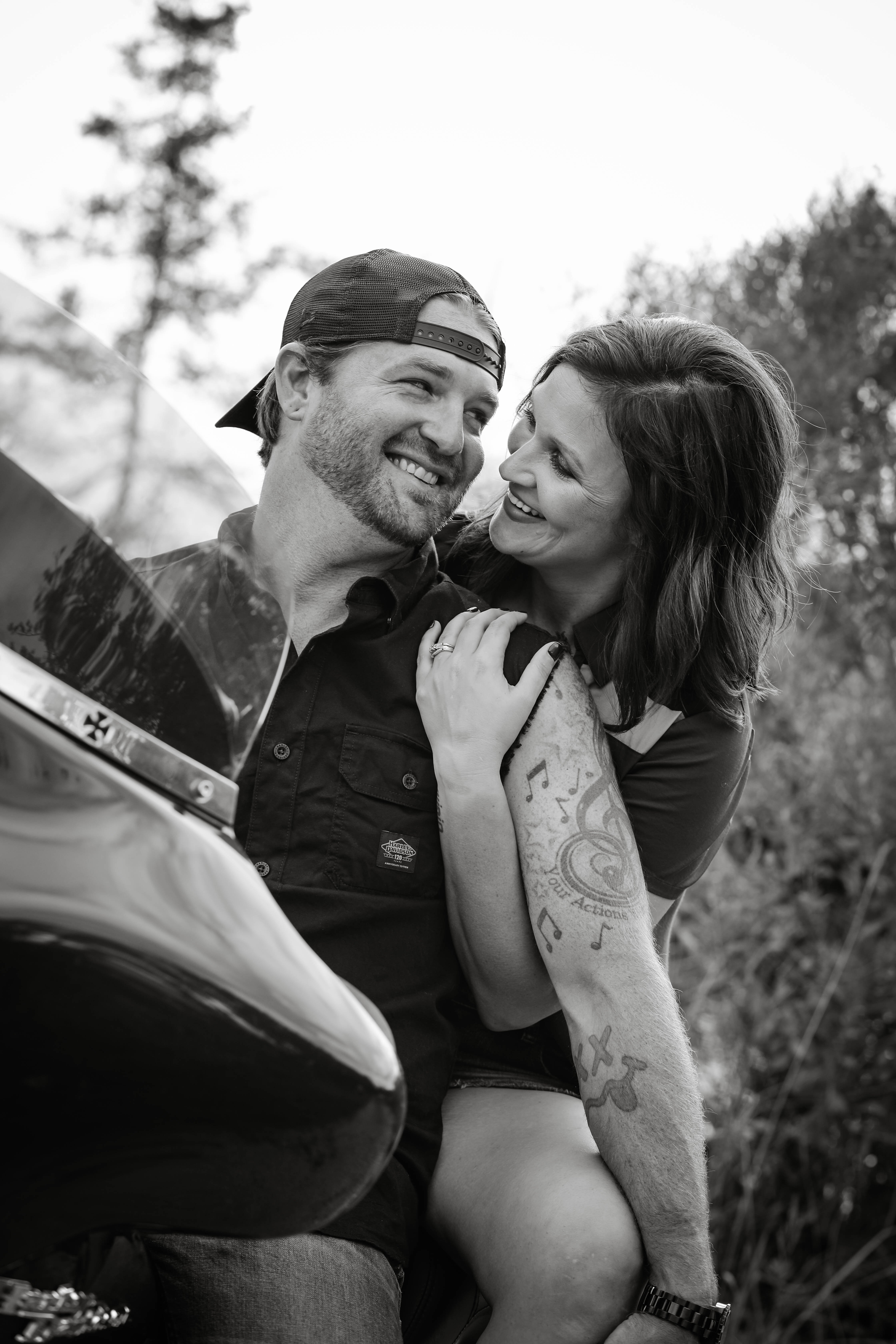 Tara and Alex sitting on a Harley smiling at each other.